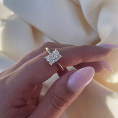 a woman's hand with a diamond ring on top of her finger and white fabric in the background