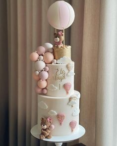 a three tiered cake with balloons and teddy bears on the top is decorated in pastel colors