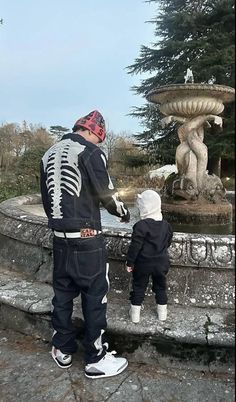 a man standing next to a little boy near a fountain with a skeleton on it