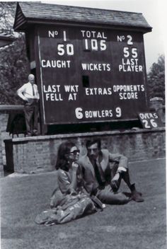 three people sitting on the ground in front of a scoreboard