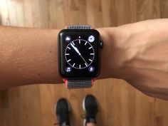 an apple watch on someone's arm showing the time and its features, with two pairs of feet in the background