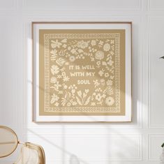 a cross stitch pattern hanging on the wall next to a chair and potted plant