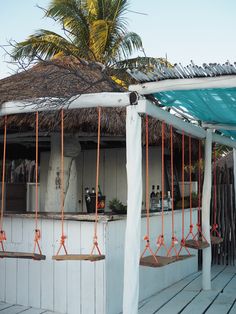 an outdoor bar with swings and palm trees in the backgrouds, on a wooden deck