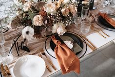 the table is set with black and white plates, silverware, gold cutlery, and flowers