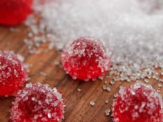 three pieces of red fruit sitting on top of a wooden cutting board covered in sugar