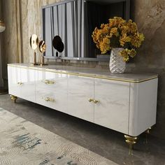 a white and gold dresser with flowers on top in front of a large mirror above it