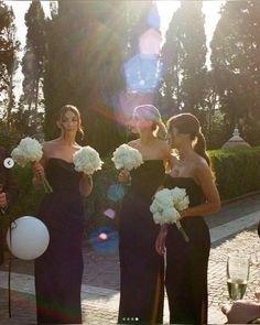 three women in black dresses holding white flowers