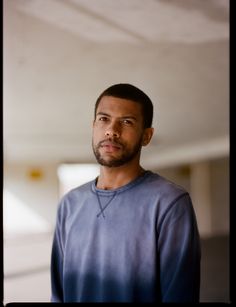 a man in a blue shirt is looking at the camera while he stands with his head turned to the side