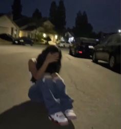 a person sitting on the ground in front of some cars at night with their hands over their face