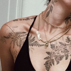 a woman with tattoos on her chest wearing a black tank top and gold chain necklace