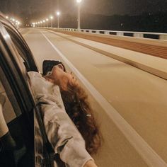 a woman laying her head out the window of a car on a highway at night