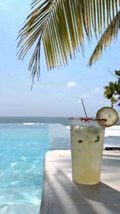 a drink sitting on top of a white table next to the ocean with a slice of lime