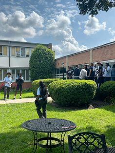 a group of people standing in front of a brick building on top of a lush green field