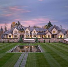 a large house sitting on top of a lush green field next to a pond in front of it