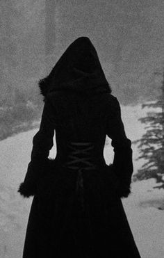 a woman standing in the snow with her back to the camera, wearing a long black coat