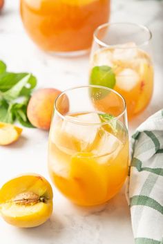 two glasses filled with orange juice and mint garnish on a marble surface next to fresh peaches