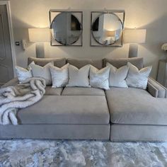 a couch with pillows and blankets on it in front of two mirrors above the couch