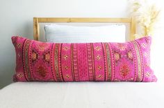 a pink pillow sitting on top of a white bed