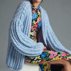 a woman sitting on top of a white chair wearing a blue knitted cardigan