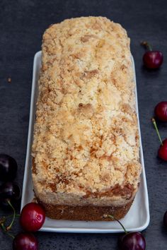 a loaf of bread sitting on top of a white plate next to cherries in the background