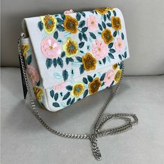 Adorable Woven Clutch Boasts Beaded, Embroidered Flowers In Hues Of Pink, Light Yellow, Mustard Yellow, And Green Throughout The Foldover Silhouette. Magnetic Closure To Reveal A Roomy, Lined Interior Complete With A Sidewall Pocket While A Silver Shoulder Chain Makes It Easy To Style Handsfree As A Crossbody. Lined. Bag Measures 9" Wide, 7" Tall, And 2" Deep (Relaxed). 43.5" Silver Chain Strap. Strap Has A 20" Drop. 70% Cotton, 10% Polyester, 10% Acrylic, 10% Iron. White Rectangular Shoulder Bag With Handwork, White Embellished Bag For Everyday Use, White Embellished Bags For Summer, White Embellished Summer Bags, Summer White Embellished Bags, White Embroidered Shoulder Bag For Summer, White Handwork Rectangular Shoulder Bag, White Embroidered Bags For Spring, Summer White Embroidered Shoulder Bag