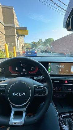 the interior of a car with an electronic display and steering wheel control, in front of a parking lot