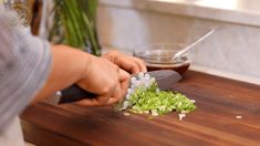 a person chopping green onions on a cutting board with a knife and seasoning