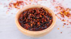 a wooden bowl filled with lots of red chili flakes on top of a white table