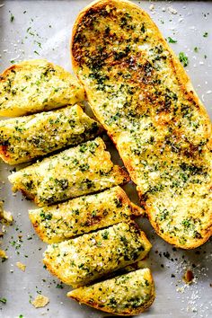 sliced bread with herbs and seasoning sitting on a baking sheet, ready to be baked