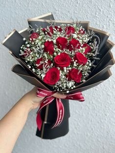 a bouquet of red roses is held up by someone's hand with a ribbon around it