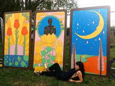 a woman laying on the ground in front of three colorful art panels with trees and flowers