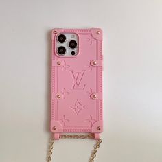 a pink phone case with chains attached to it on a white surface and a gold chain hanging from the back