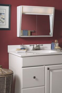 a bathroom vanity with a mirror above it and a sink under the counter top in front of a red wall