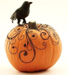 a small black bird sitting on top of a pumpkin with swirls and scrolls painted on it