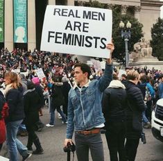 a man holding up a sign that says real men are feminists in front of a crowd