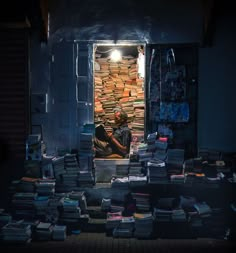 a man sitting in the doorway of a book store with stacks of books all around him