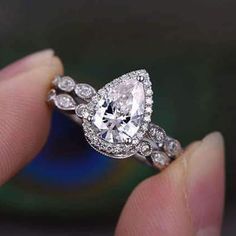 a woman's hand holding an engagement ring with a pear shaped diamond on it