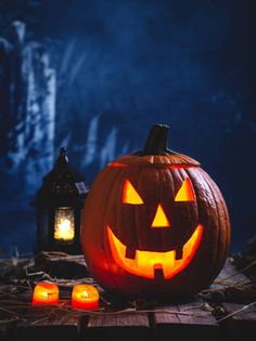 a carved pumpkin sitting on top of a wooden table next to two lit candles and a lantern