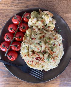 a plate with pasta, tomatoes and shrimp next to a fork on a wooden table