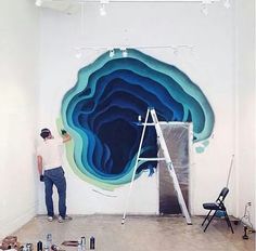 a man standing on a ladder in front of a large blue piece of art that is being worked on