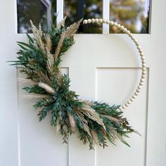 a wreath hanging on the front door of a house with beads and greenery around it