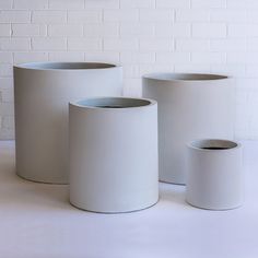 three white vases sitting next to each other in front of a white brick wall