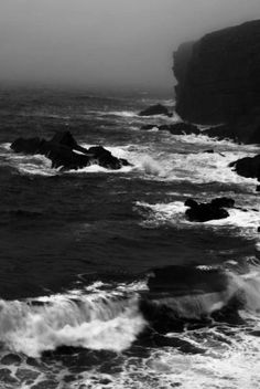 the ocean is green and choppy as it comes towards shore with large rocks in the foreground