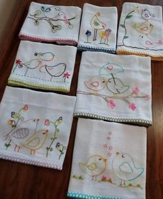 nine embroidered napkins with birds on them sitting on a wooden floor next to a window