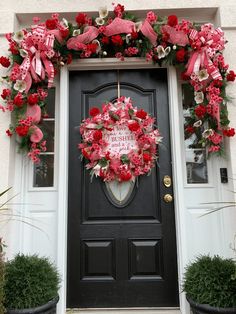 a black front door decorated with pink and red flowers, greenery and a heart shaped wreath