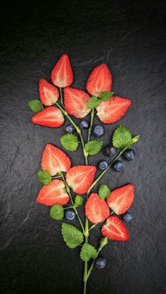 strawberries and blueberries are arranged on a black surface with green leaves, berries and mint