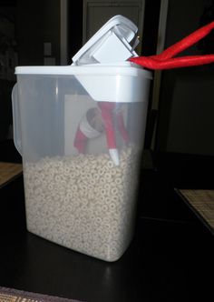 a plastic container filled with lots of oats on top of a wooden table next to a red ribbon