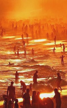 many people are standing on the beach at sunset or sunrise, with orange and yellow hues