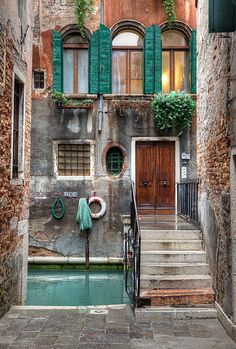 an old building with green shutters on the windows and stairs leading up to it