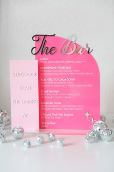 a pink and black wedding menu on a table with silver foiled balls in the foreground